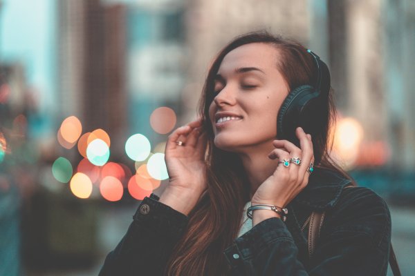 bluetooth wireless wired headphones woman long hair happy closed eyes listening to music on headphones city lights in the background